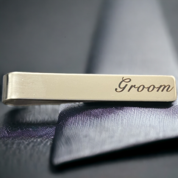 A tie clip on a black background reading 'Groom'