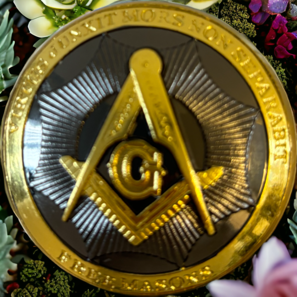 A masonic emblem in grey and gold from the top of a masonic walking stick surrounded by flowers and leaves.