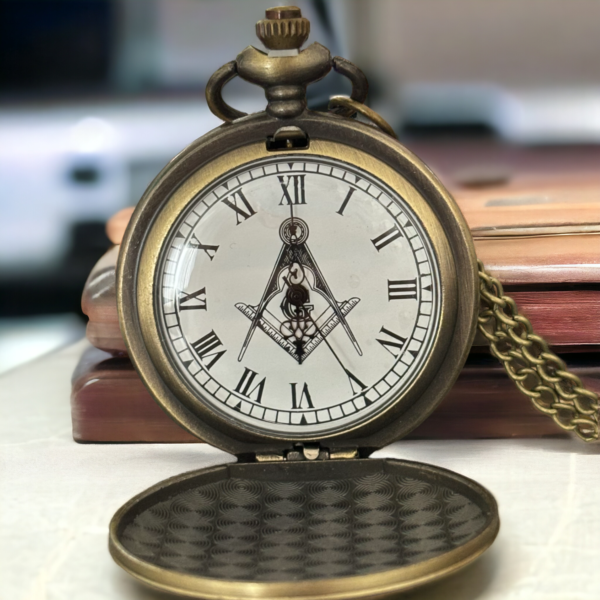 An open pocket watch resting on a white desk leaning on a book.