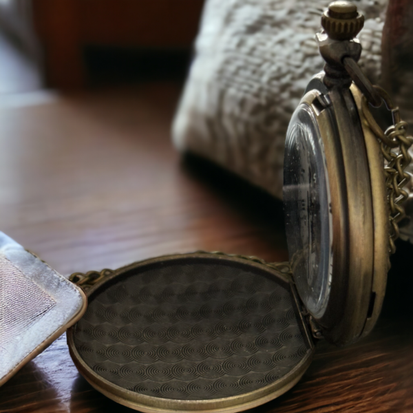 the side view of a masonic pocket watch on a wooden desk with a sliver cushion in the background and a silver cloth lying over a tiny portion of the front.