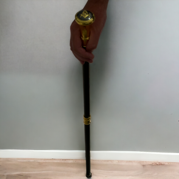 A masonic walking stick being held against a light grey background on a light wooden floor.