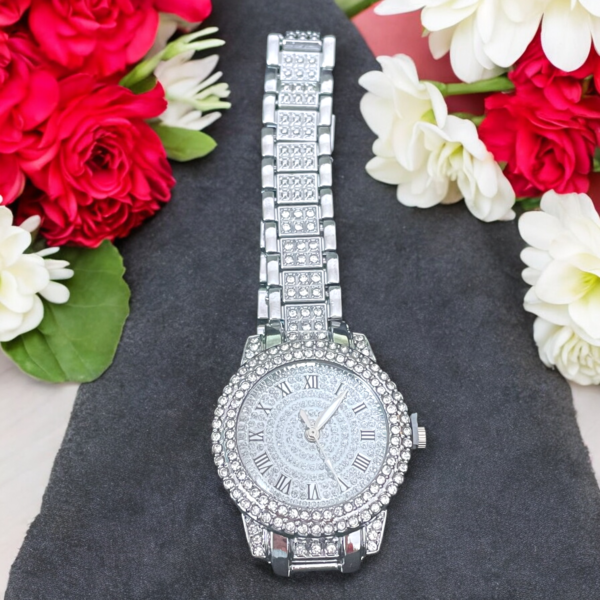 A rhinestone encrusted ladies watch on a black velvet cushion with red and white flowers